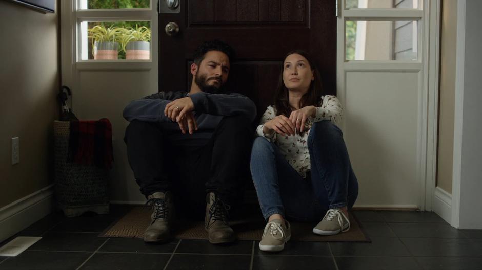 Dave and Carmen sit on the ground in the entryway leaning against the front door.