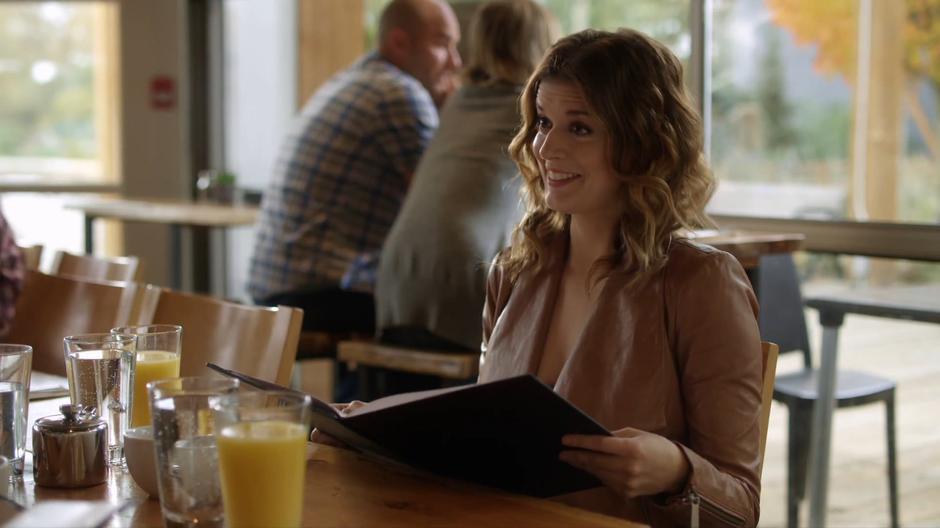 Izzy smiles up at Jack and Emma while looking at the menu.