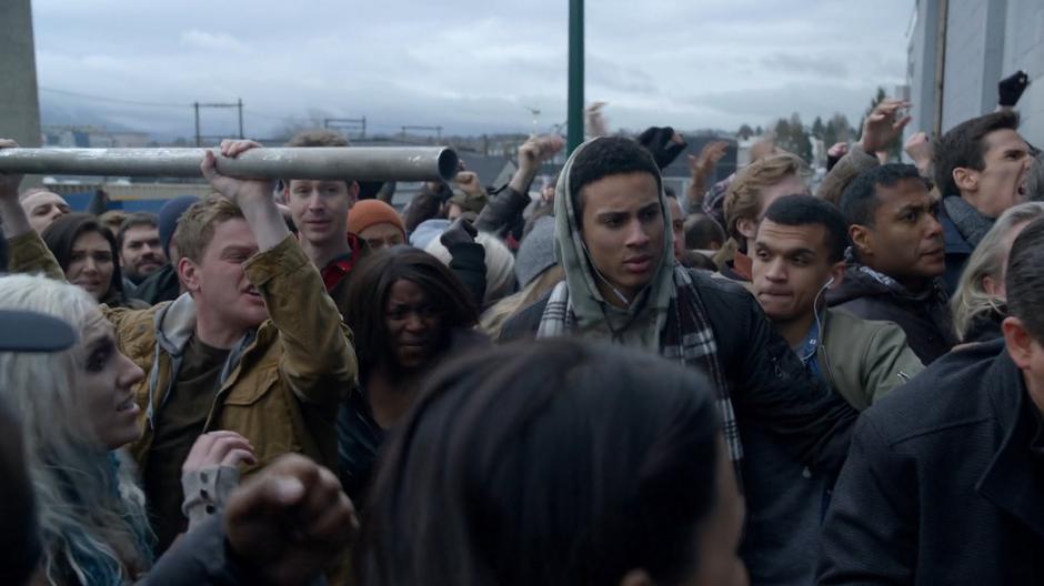 Stan passes a metal pole up to the front of the mob to help open the door.