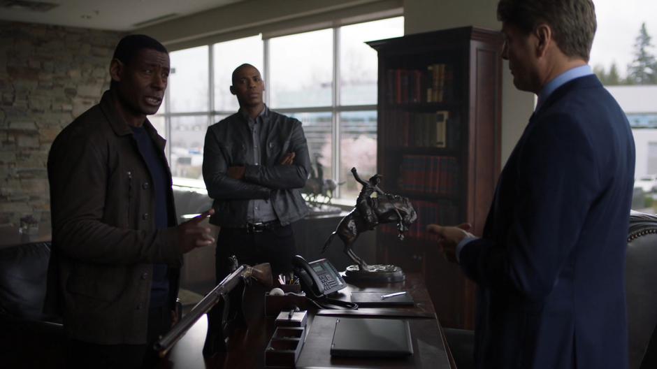 J'onn lays down the law to the CEO while James watches.