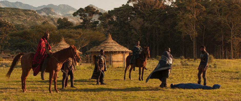 W'Kabi walks up to Killmonger to examine the body while his guards watch closely.