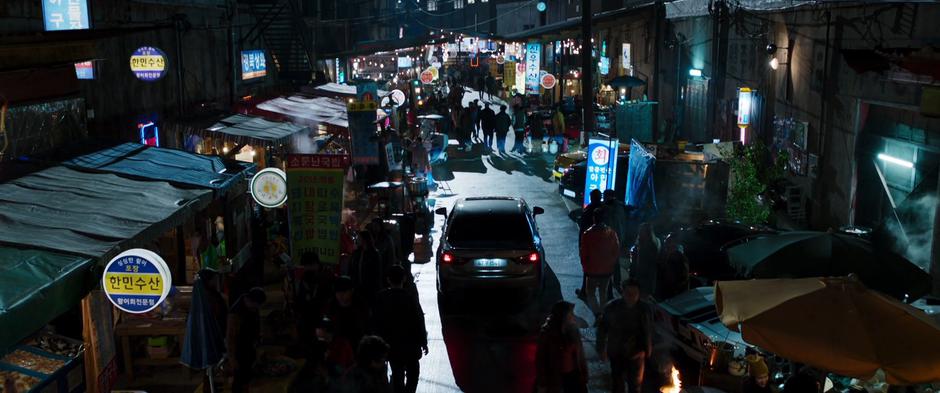 A car drives down the center of the busy night market.