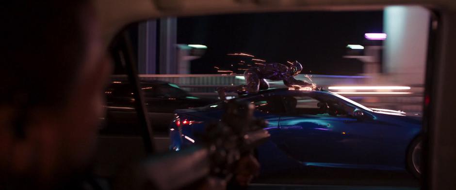 The goon fires at T'Challa as his car pulls up alongside the SUV.