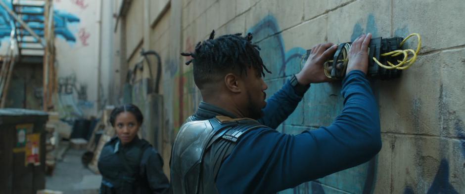 Linda watches as Killmonger plants the breaching explosive on the wall.