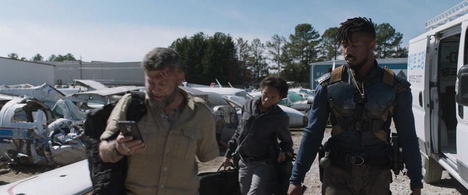 Ulysses Klaue, Linda, and Killmonger carry their gear over to the plane from the van.