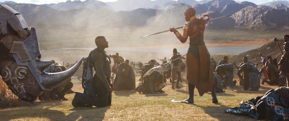 W'Kabi kneels down in front of Okoye who holds him at spearpoint.