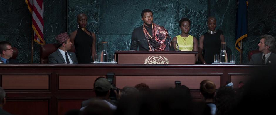 Okoye, Nakia, and Ayo stand behind T'Challa as he begins his speech.