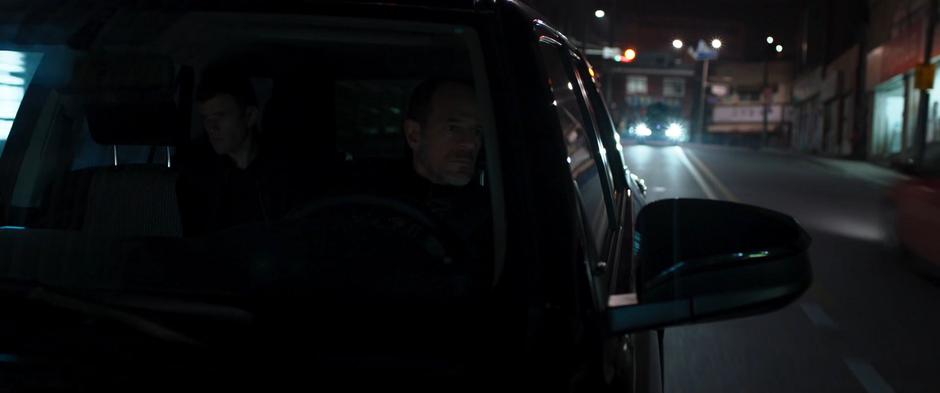 One of the drivers of the SUVs looks in his side mirror at T'Challa following on the roof of a car.