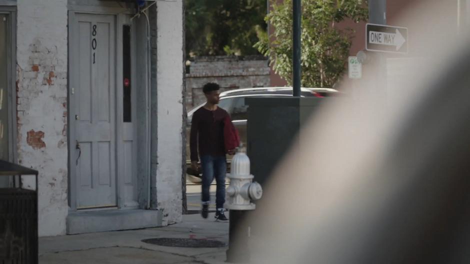 Tyrone walks around the corner with the red bag he stole from the dealer.