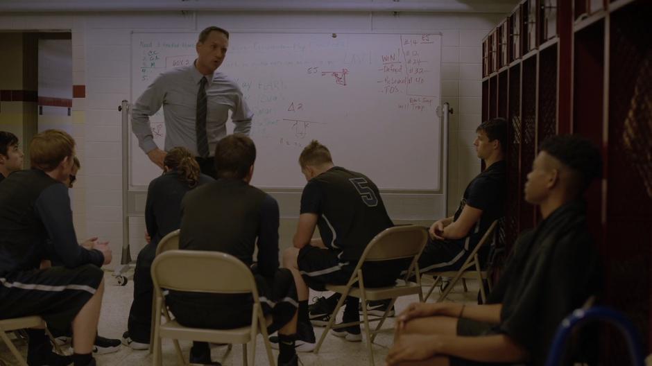 Tyrone watches as his coach addresses the team in the locker room.