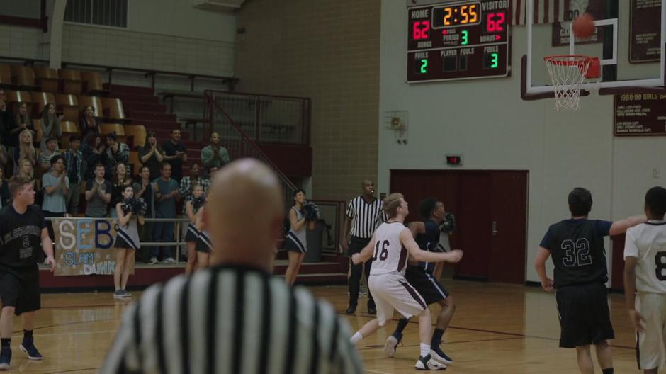 Tyrone guards his matching player on the other team while the ball flies towards the basket.