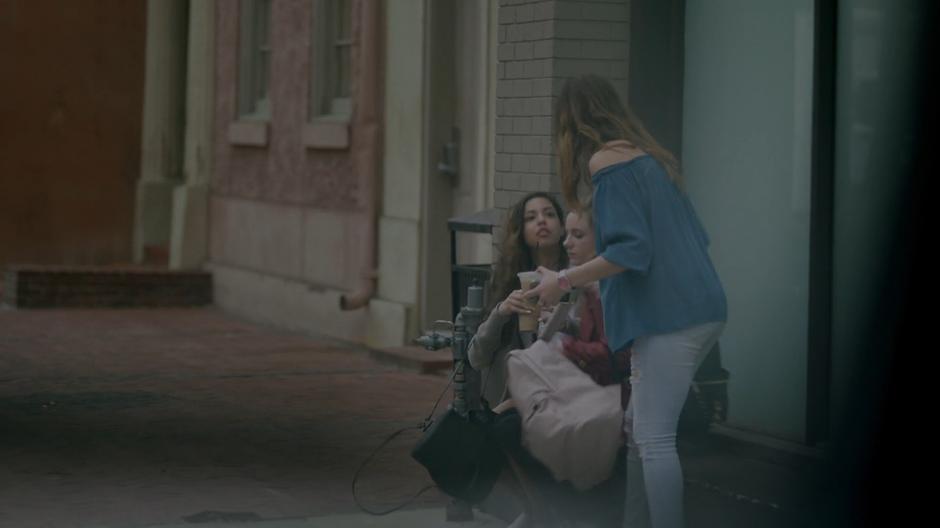 Several young women are visible handing out on steps down the street from the car.