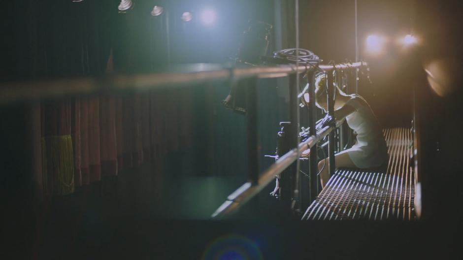 Tandy sits on the catwalk above the stage and watches the dancers down below.