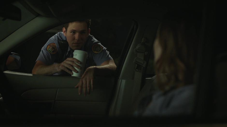 An officer leans into the window of O'Reilly's car to bring her coffee.