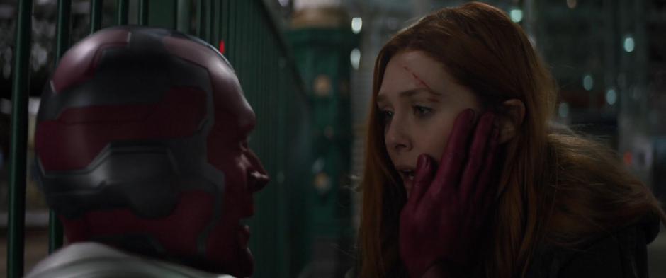 Vision puts his hand on Wanda's cheek as she kneels down over her.