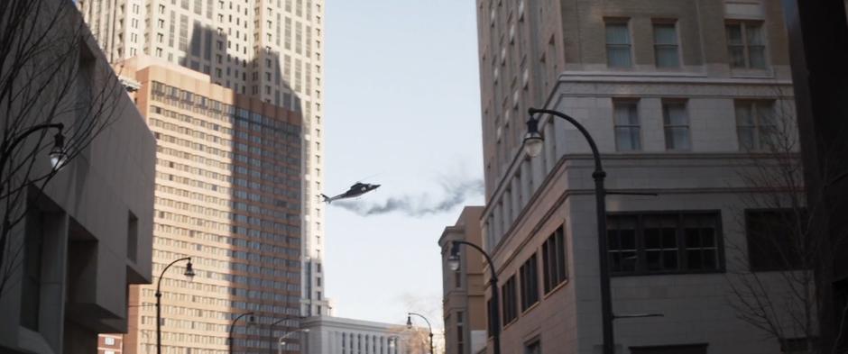 A helicopter flies out of control through the air towards a building while trailing smoke.