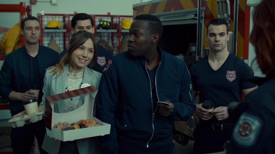 Waverly smiles at Nicole while talking to the fire fighters and holding the box of donuts.