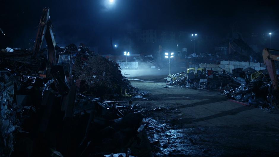 Establishing shot of the junkyard lit by portable lights.