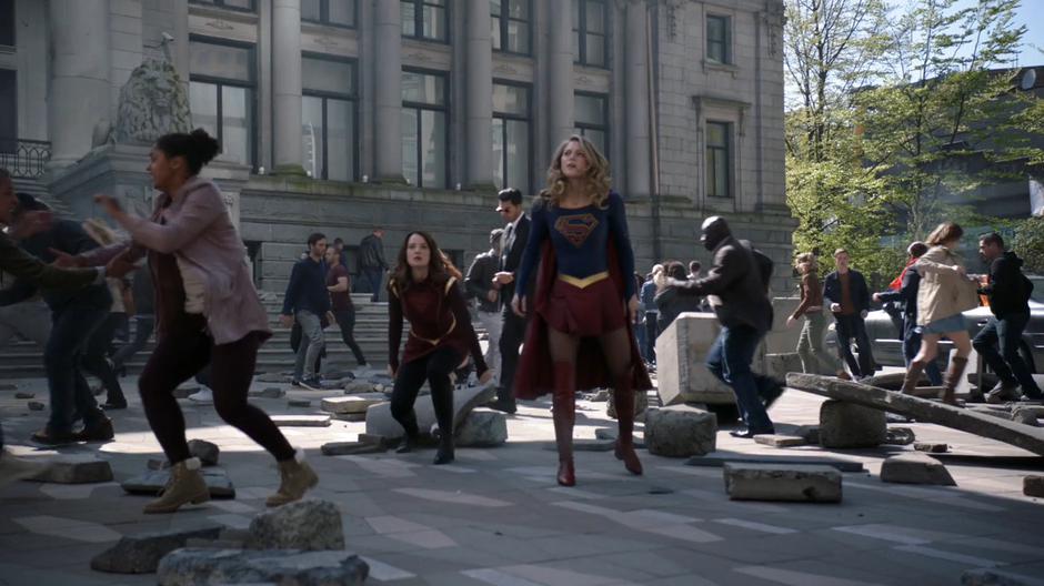 Alura and Kara land in the plaza as debris rains down from the sky.