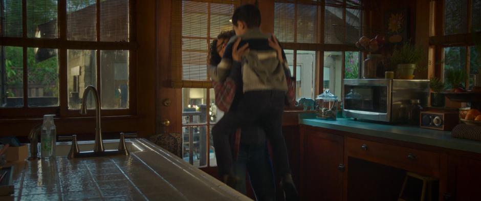 Meg lifts Charles Wallace into the air to hug him in the kitchen.