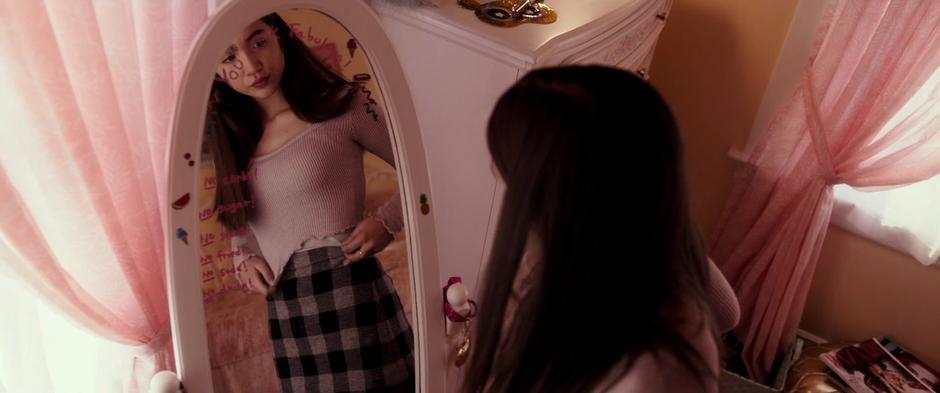 Veronica examines herself in her bedroom mirror.
