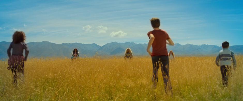 Meg, Calvin, and Charles Wallace run across the field towards Mrs. Who, Which, and Whatsit.