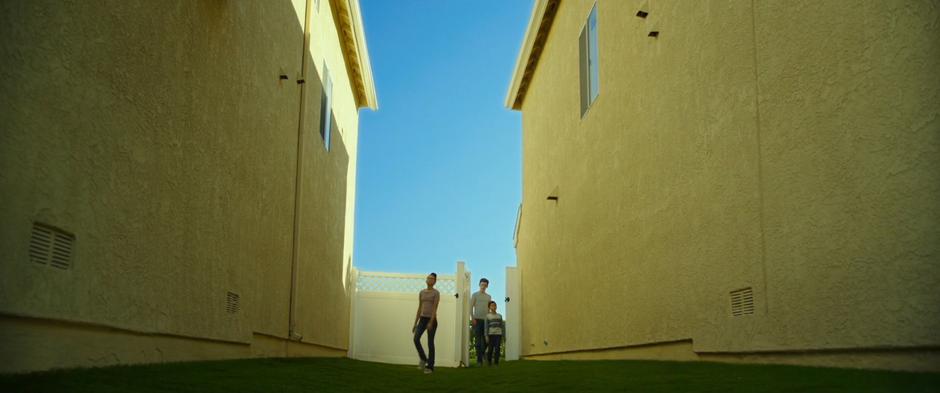 Meg, Calvin, and Charles Wallace walk through a gate between two houses.