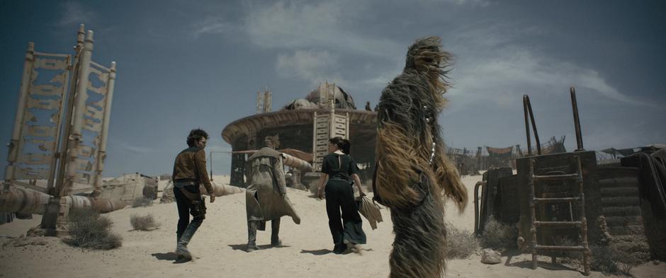 Chewbacca glances back down the hill as he walks up with Han, Beckett, and Qi'ra.