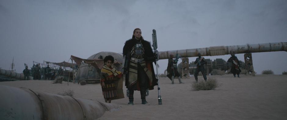 Enfys Nest holds the hand of a young local while watching Han and Chewie approach.