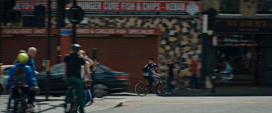 Lara rides her bike down the street past a fish & chips shop.