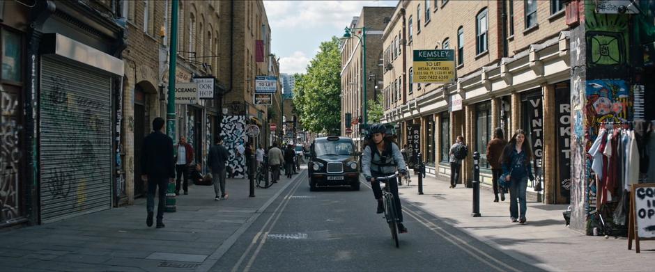 Lara turns her bike off the road towards the alley.