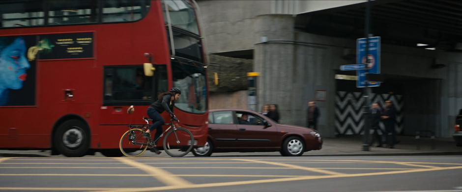 Lara bikes around a double-decker bus and under a bridge.