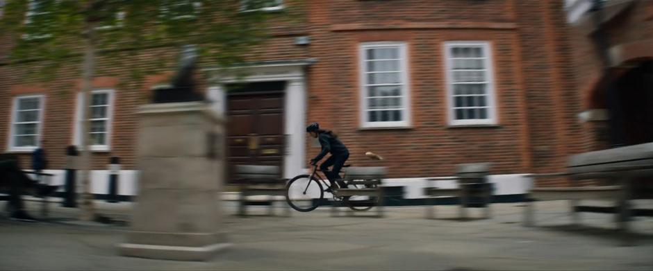 Lara rides past a brick building through the courtyard.