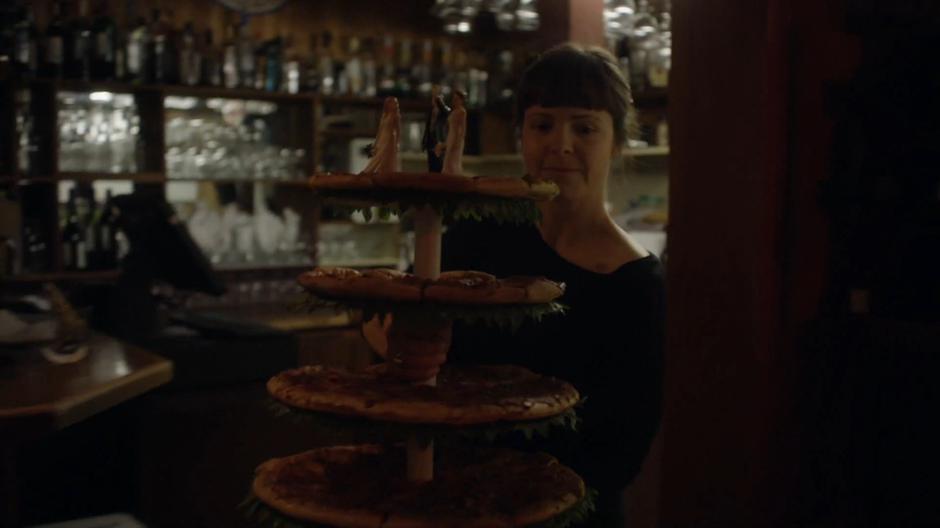 The woman front the restaurant comes out carrying a tower of pizza with three wedding cake toppers.