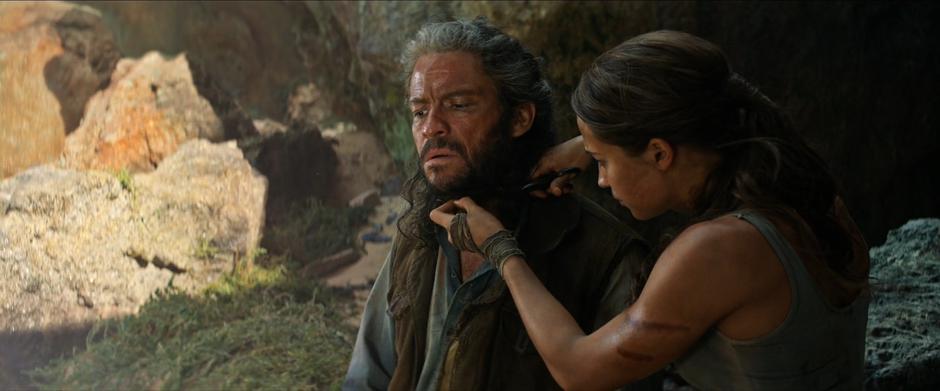 Lara cuts her father's beard outside the cave entrance.