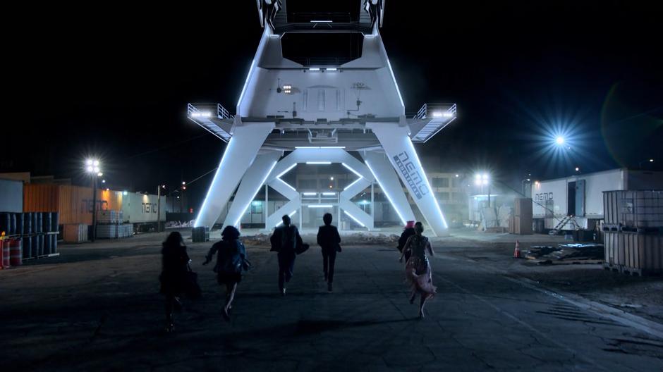 The teens run across the construction site in the evening where the drill stand sits empty.