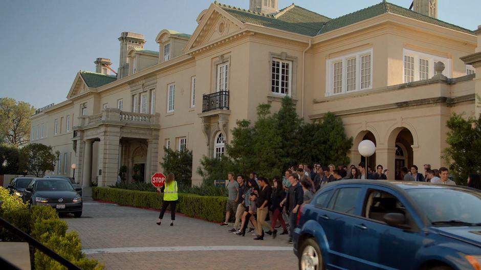 A crossing guard stops traffic in front of the school to let a crowd of students cross the street.