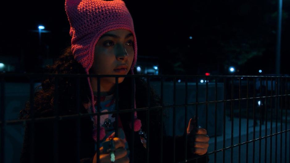 Molly holds onto the fence surrounding the station and looks over at the lockers.