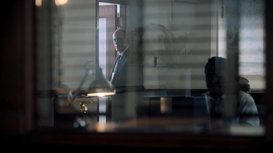 Detective Flores glances over as he enters his office.