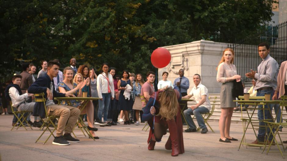 Kara lands in the plaza holding the balloon.