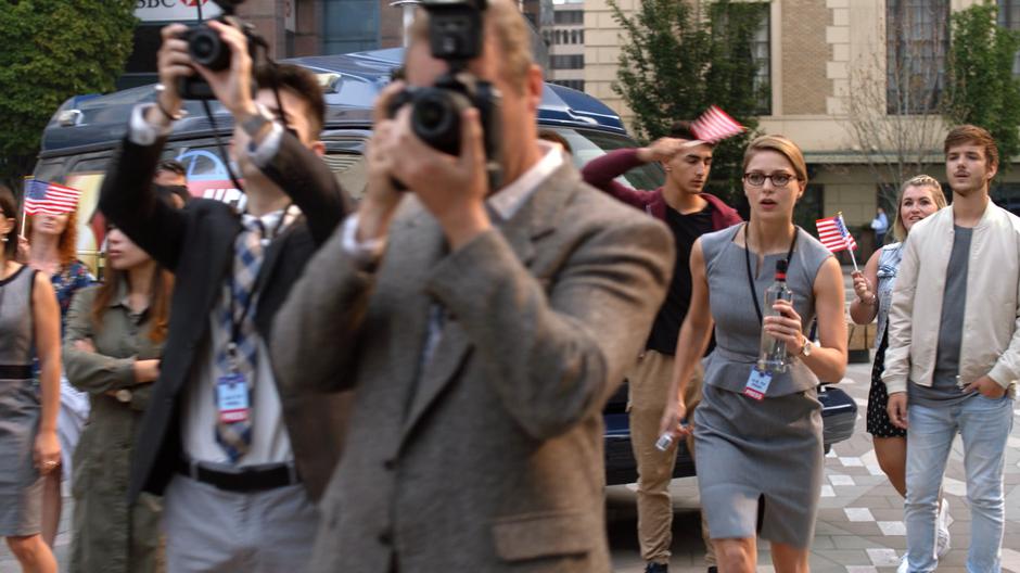 Kara pushes her way through the crowd of reporters as the press conference begins.