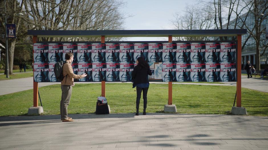 Cam approaches Mel as she is hanging up posters in the middle of campus.