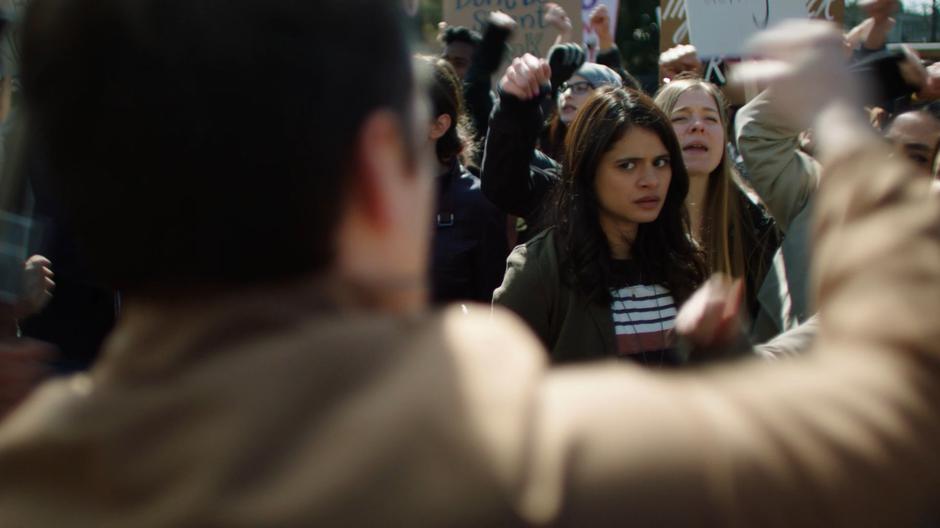 Mel makes eye contact with Cam from opposing sides of the protest.