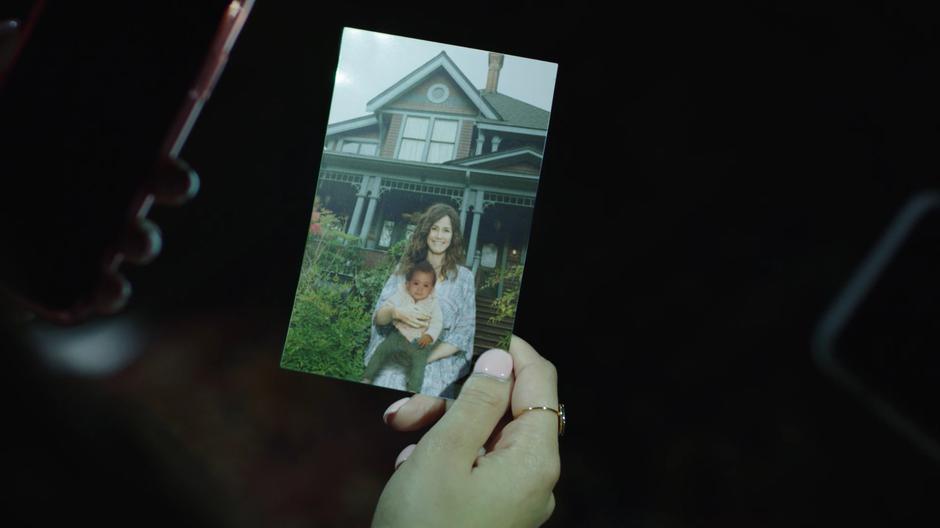 Macy shows her sisters a photo of her with her mother in front of the house when she was a child.