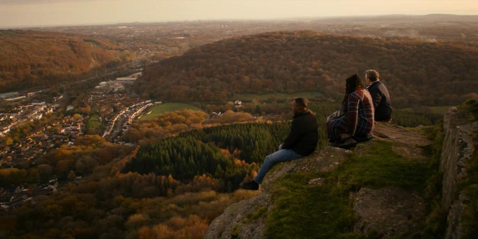 Ryan, Grace, and Graham sit on the edge of the cliff and talk while looking out over the scenery.