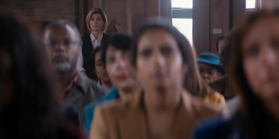 The Doctor watches the eulogy from the back of the church.