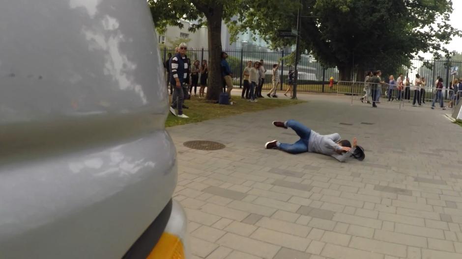 A man falls to the ground in front of the path of the news van.
