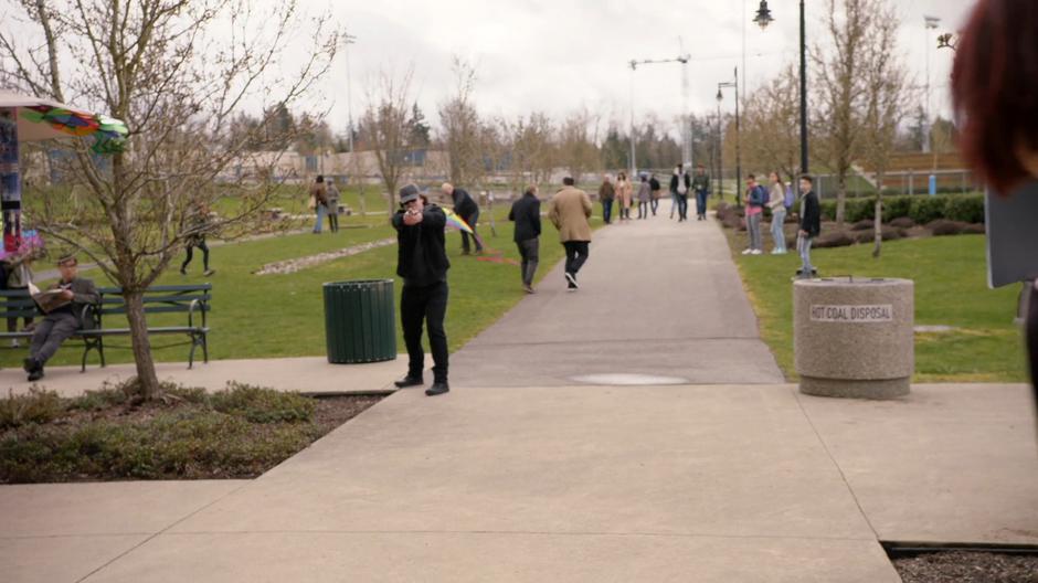 A man points a gun at Alex from across the path.