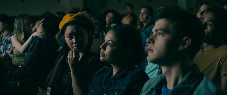 Lara Jean looks over at Margo and Josh as they watch the movie.