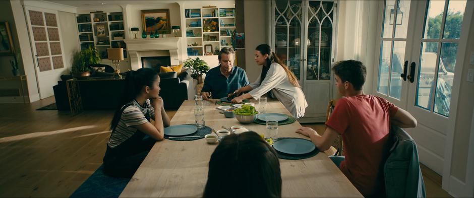 Margo takes the burnt food that her father was trying to cut while Lara Jean, Kitty, and Josh watch.